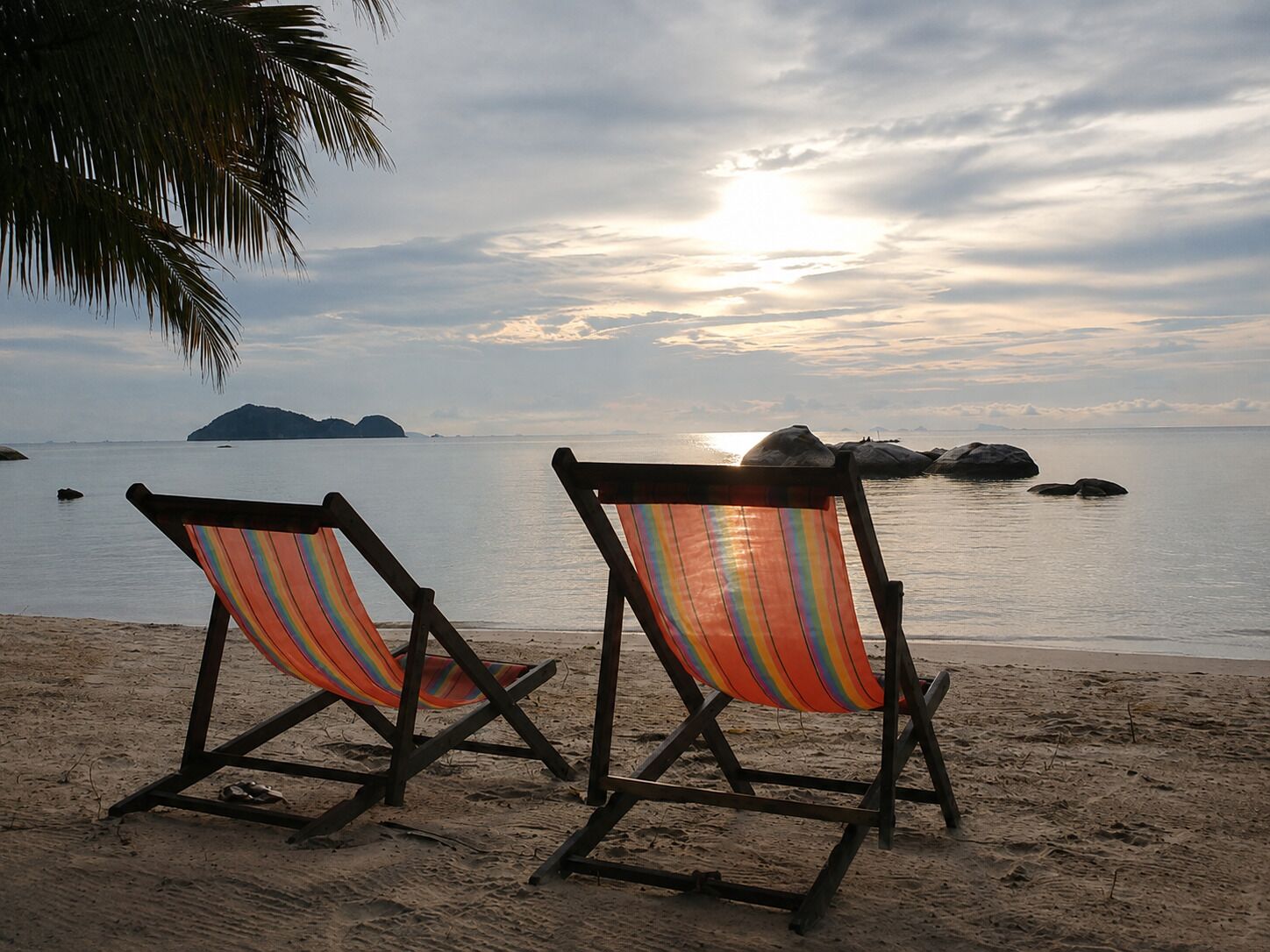 Dos sillas de playa mirando al mar, con un atardecer de fondo.