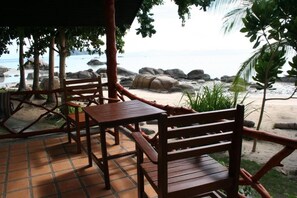 Un conjunto de mesa y sillas de madera bajo una zona sombreada con vista a la playa y al océano.