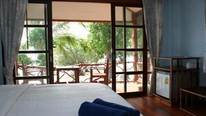 Quarto de hotel com cama, vista para área externa com mesas e cadeiras, e uma pequena mesa com uma cadeira no quarto.