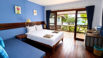 A hotel room with a large bed, a smaller bed, a wooden nightstand, a table with a lamp, and a view of the outdoors.