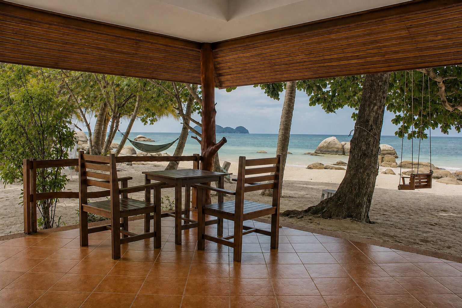 A beachside seating area with a wooden table and chairs, overlooking a sandy beach and the ocean.
