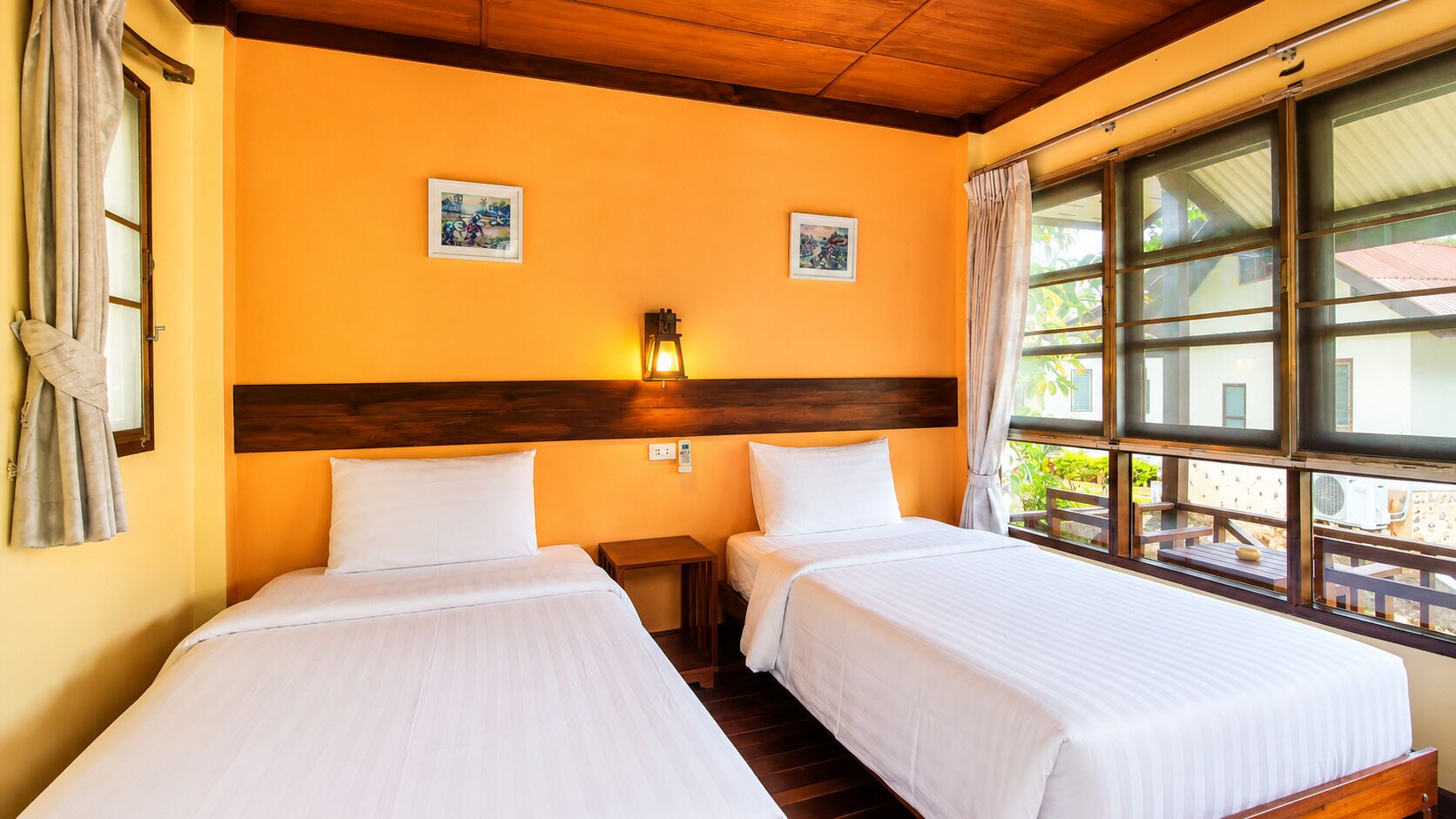 Quarto de hotel com duas camas, cabeceira de madeira, obras de arte na parede e janela com vista.