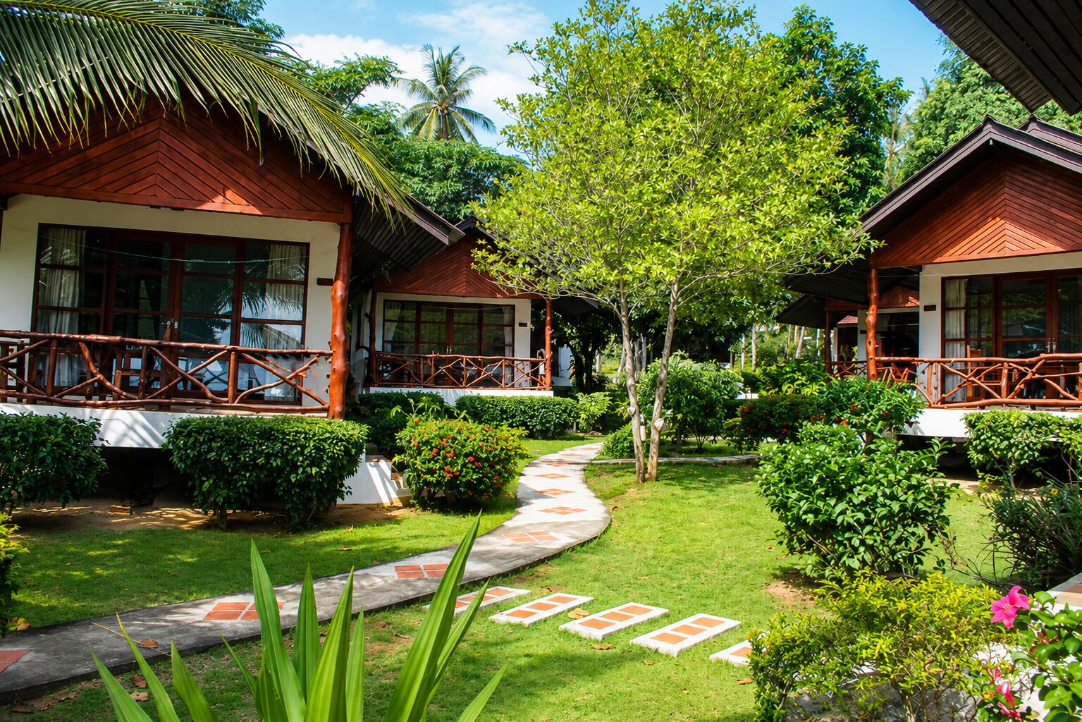 A bungalow-style hotel with a thatched roof, surrounded by lush greenery and a well-maintained garden.