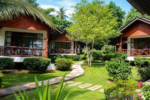 Un hotel de estilo bungalow con techo de paja, rodeado de exuberante vegetación y un jardín bien cuidado.