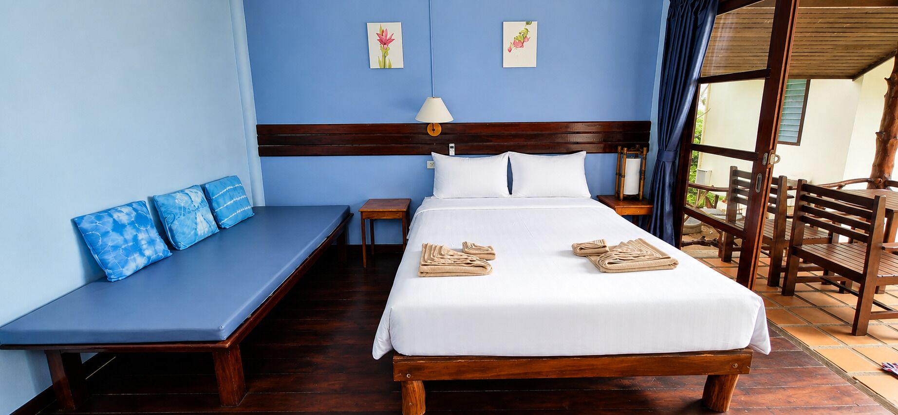 Una habitación de hotel con una cama, un banco, una mesita de noche y vistas al exterior.