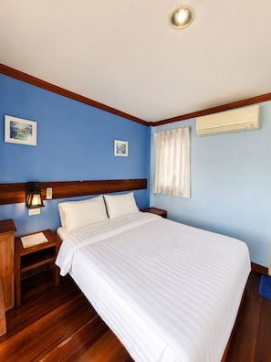 Una habitación de hotel con cama, mesitas de noche, aire acondicionado de pared y dos cuadros enmarcados.