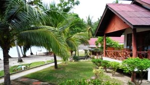 Um resort tropical com um edifício de madeira, palmeiras e um gramado bem cuidado.