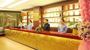 Un comptoir d’accueil d’hôtel avec du personnel, un mur décoratif et des étagères contenant divers objets.