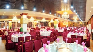 Une salle de banquet avec des tables rondes, des chaises rouges et des lustres.