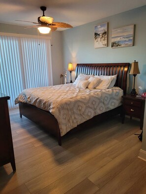 Une chambre à coucher avec un lit en bois, un ventilateur de plafond, une table de chevet avec une lampe et une fenêtre avec des stores.