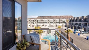 A balcony with a view of a pool, a building in the background, and a parked car.