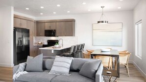 A modern kitchen with built-in appliances, a dining area with a table and chairs, and a gray sofa in the living area.
