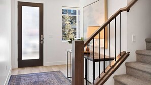A modern entryway with a dark door, a small table with a lamp, and a staircase with wooden steps and black railings.