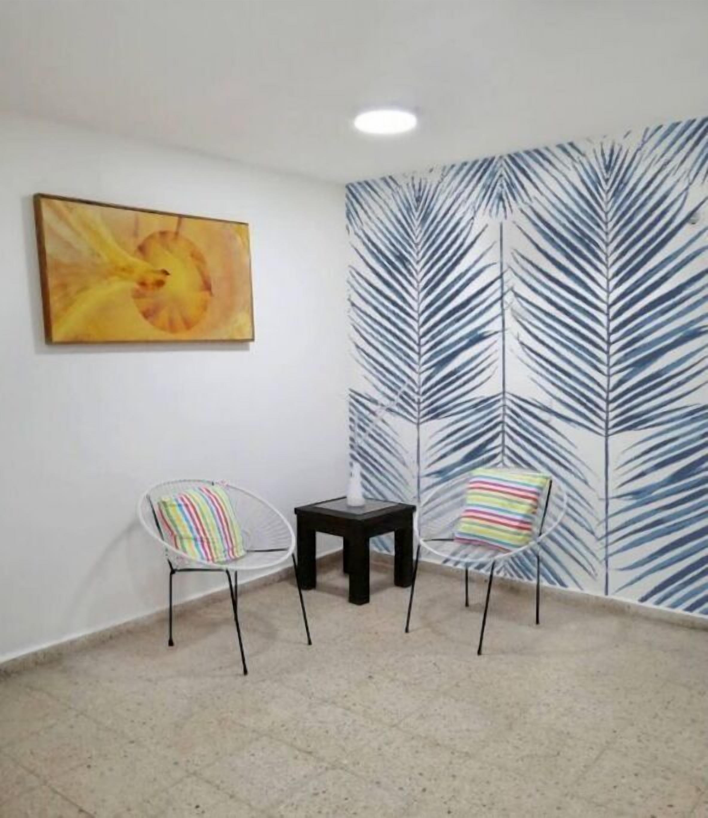 Une pièce avec deux chaises et une petite table, un tableau au mur et un papier peint à motifs de feuilles.