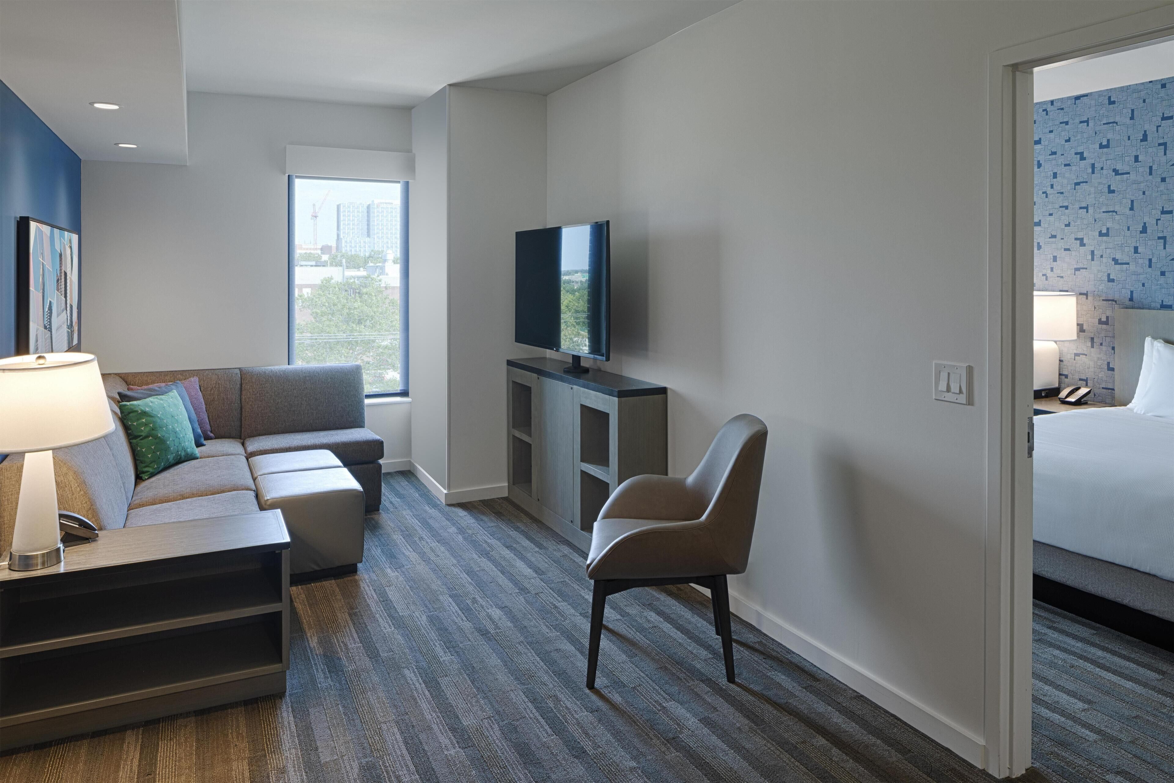 A hotel room with a sofa, armchair, television, and a bed.