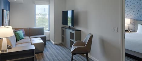 A hotel room with a sofa, armchair, television, and a bed.