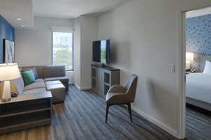 A hotel room with a sofa, armchair, television, and a bed.