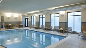 An indoor swimming pool with clear blue water, surrounded by lounge chairs and tables, with large windows providing natural light. - Hyatt House Columbus OSU / Short North (Columbus)