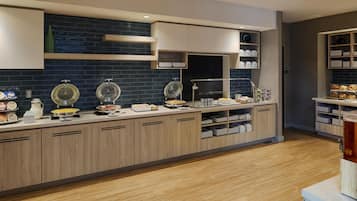 A modern kitchen with a long counter, built-in cabinets, and a variety of food items displayed.