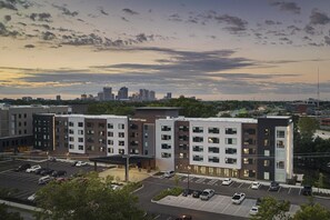 A multi-story hotel with a parking lot, surrounded by other buildings and a city skyline in the background. - Hyatt House Columbus OSU / Short North (Columbus)
