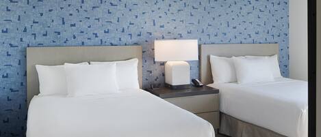 Een hotelkamer met twee bedden, een nachtkastje met een lamp en telefoon, en een kamer met een patroon op de muur.