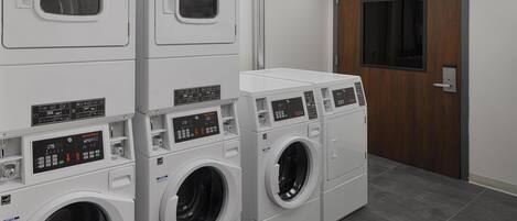 A laundry facility with multiple washing machines and dryers, a wooden door, and a tiled floor.
