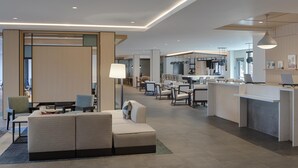 A modern hotel lobby with a seating area, a reception desk, and a kitchen in the background. - Hyatt House Columbus OSU / Short North (Columbus)