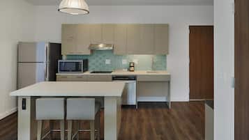 Eine moderne Küche mit Edelstahlkühlschrank, Mikrowelle und Geschirrspüler, einem Holzespeisetisch mit zwei Stühlen und einer Holztür.