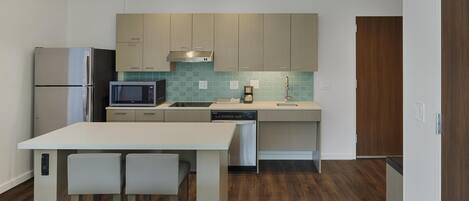 A modern kitchen with a stainless steel refrigerator, microwave, and dishwasher, a wooden dining table with two chairs, and a wooden door.