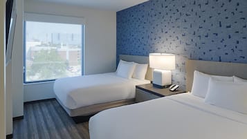 A hotel room with two beds, a large window, a wall with a geometric pattern, and a nightstand with a lamp and phone.