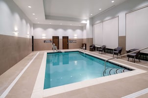 Piscina com deck revestido, cadeira de salva-vidas e área de estar com cadeiras e mesas.