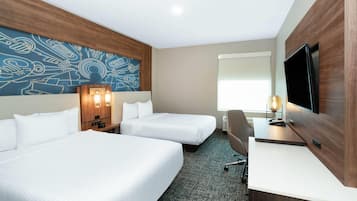 Habitación de hotel con dos camas, un escritorio, un televisor y una pared con un diseño abstracto azul.