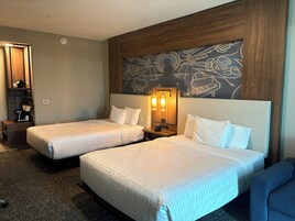 Habitación de hotel con dos camas, una mesita de noche, una lámpara de pared y un panel decorativo.