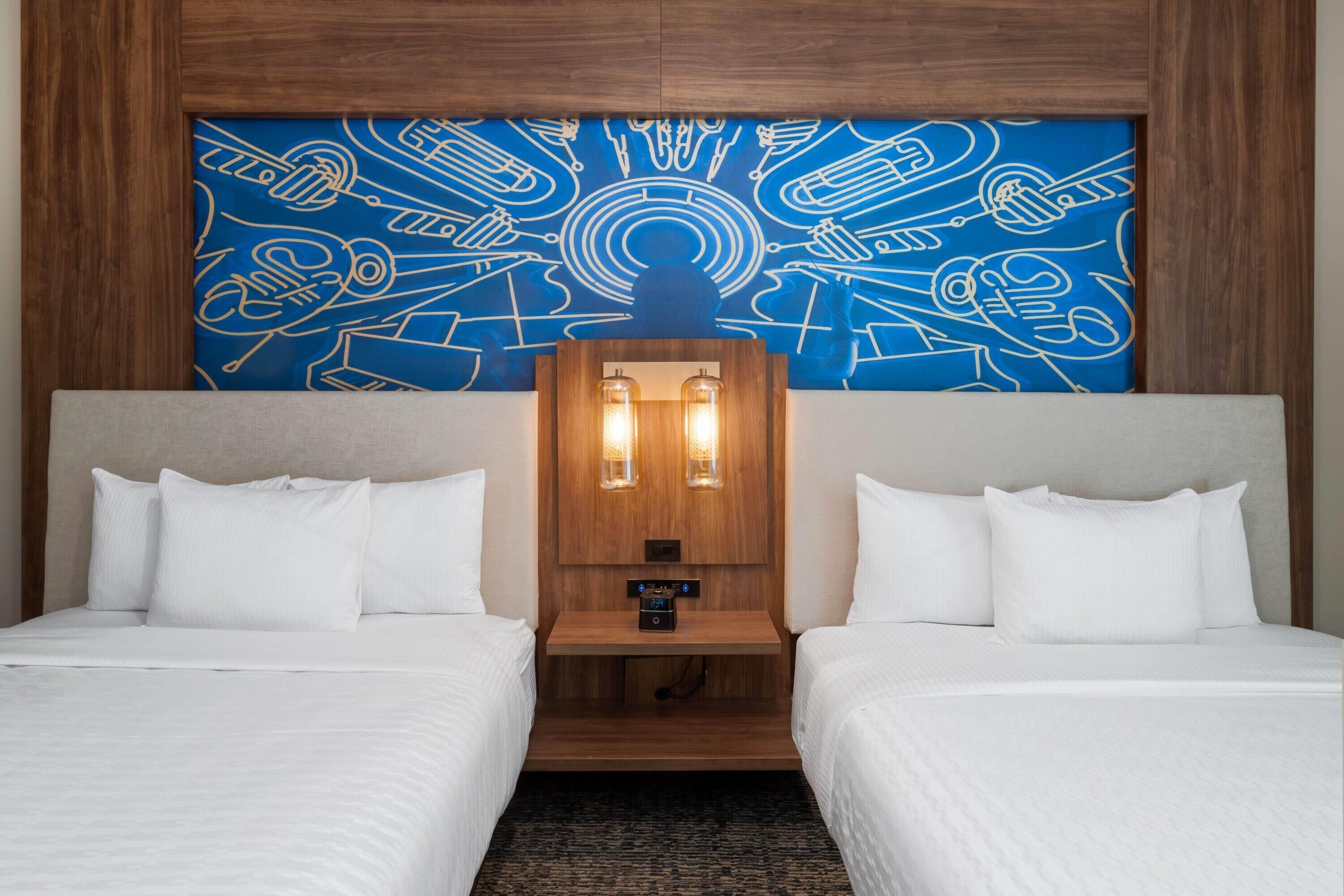 Camera d'albergo con due letti, una testiera in legno, un quadro appeso al muro e un comodino con due lampade.