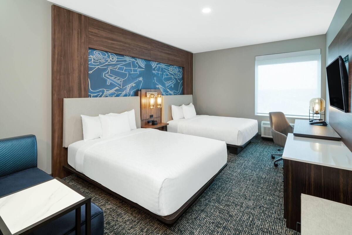 A hotel room with two beds, a desk, a chair, a TV, and a large window.