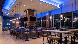 A modern bar area with a long counter, multiple stools, and a large window offering a view of the cityscape at night.