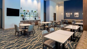 A hotel lobby with a bar area, multiple seating options including round tables and booths, and a patterned carpet.