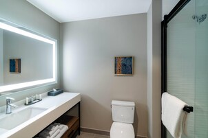 Ein modernes Badezimmer mit großem Spiegel, Waschbecken in Weiß, Toilette und einer Duschkabine aus Glas.