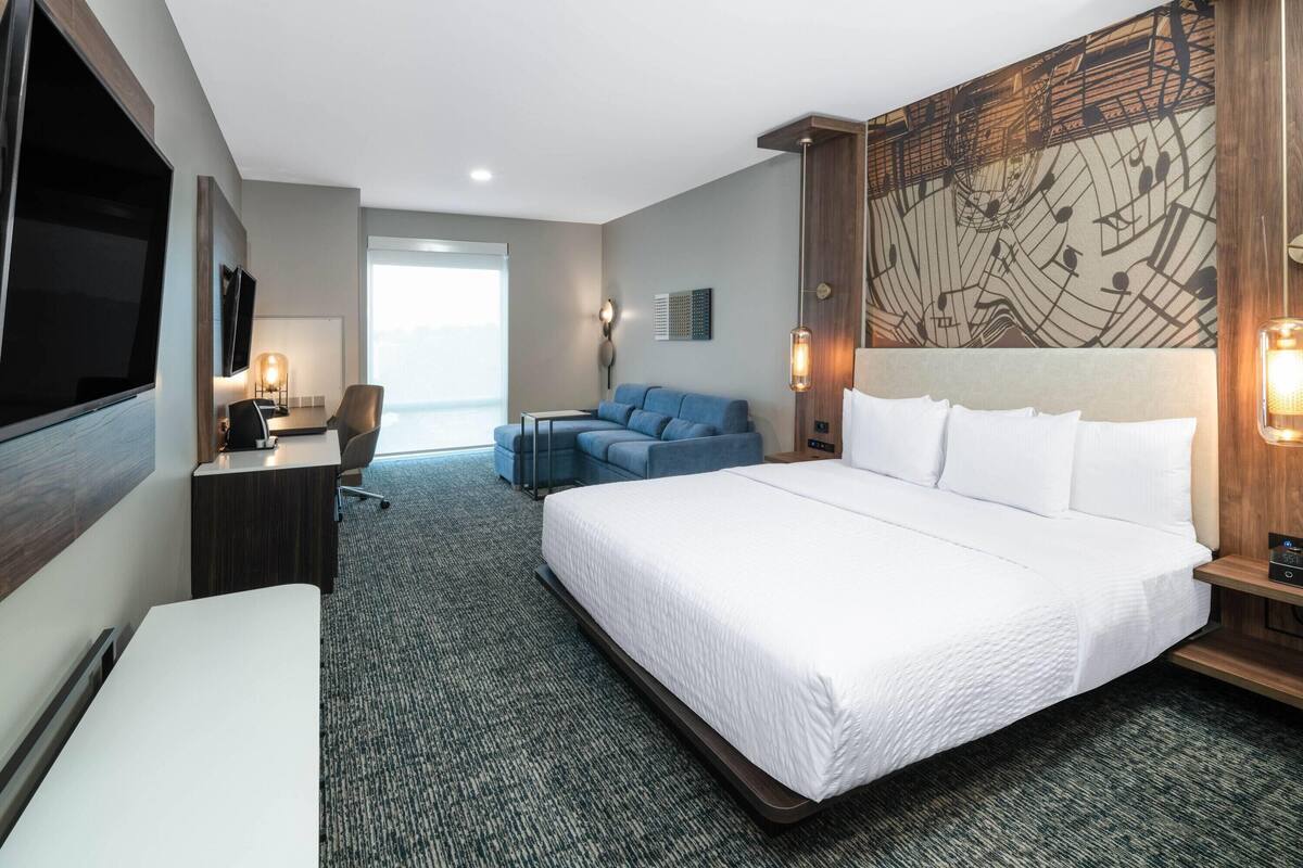 A hotel room with a large bed, a desk, a chair, a TV, and a wall with a musical note design.