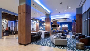A modern hotel lobby with a bar area, seating, and a large TV screen.