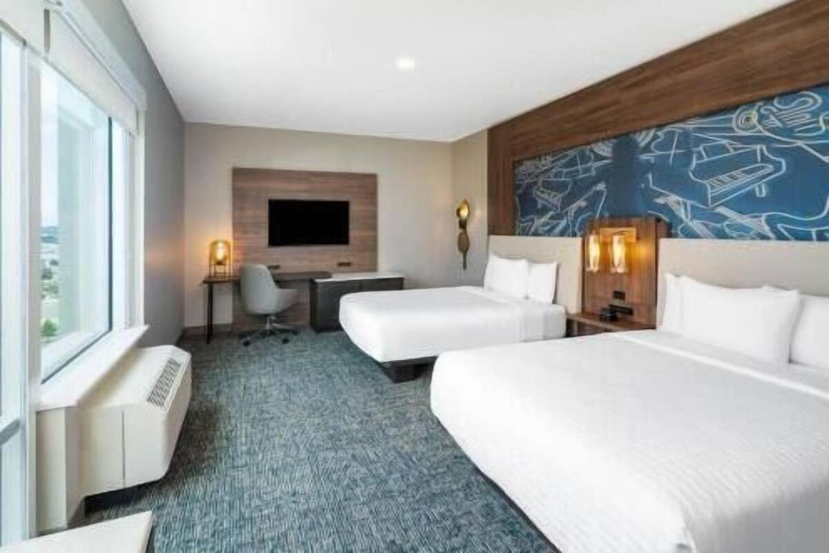 A hotel room with two beds, a desk, a chair, a TV, and a large window.