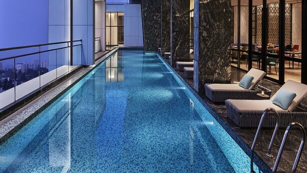 Een modern binnenzwembad met helderblauw water, ligbedden en uitzicht over de stad.