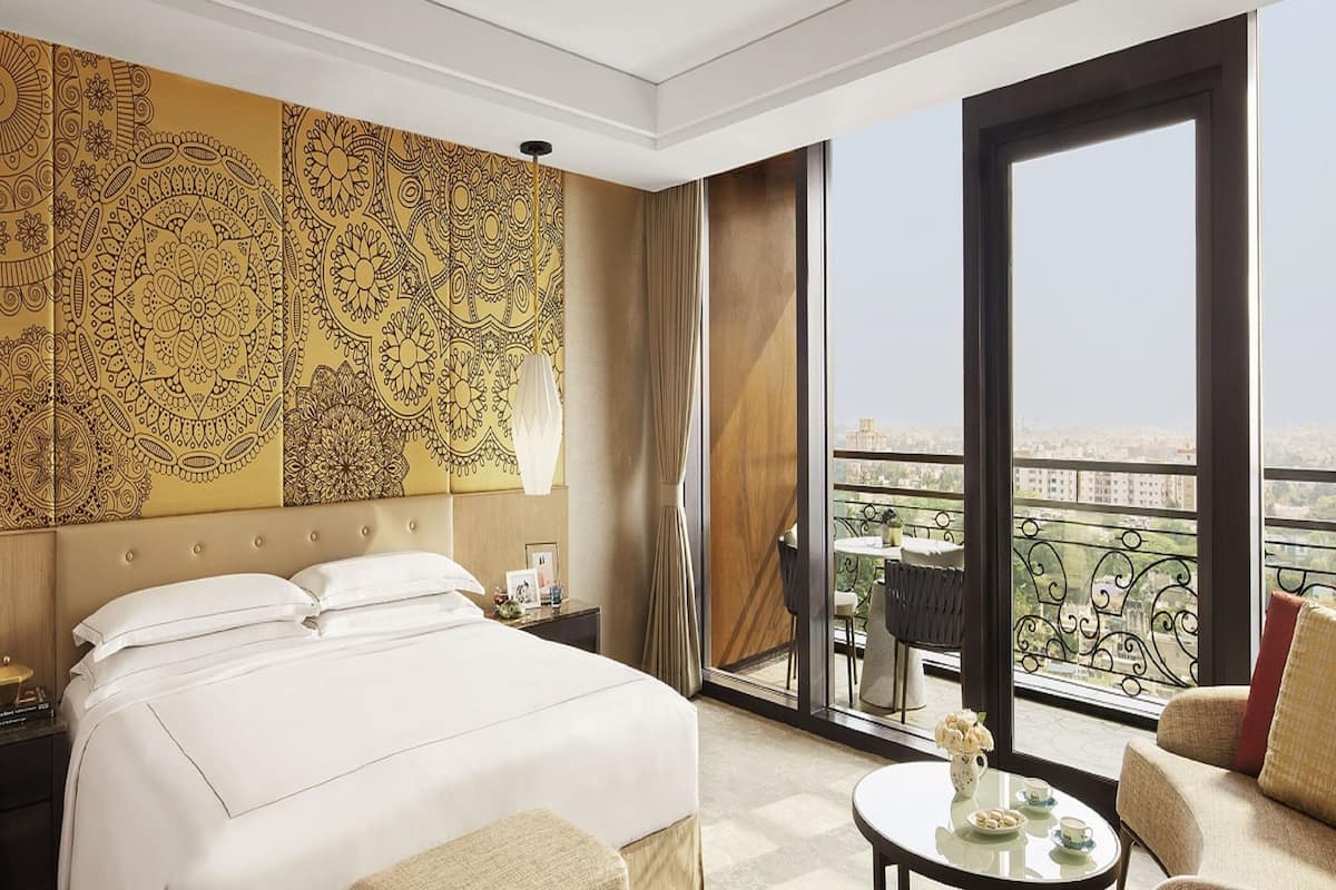 Une chambre d’hôtel dotée d’un grand lit, d’un coin salon avec une table et des chaises, et d’un balcon offrant une vue sur la ville.