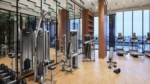 Een moderne sportschool met diverse trainingsapparaten, grote ramen en een houten vloer.