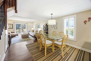 A spacious living area with a glass dining table surrounded by wicker chairs, a sofa, and a bookshelf.