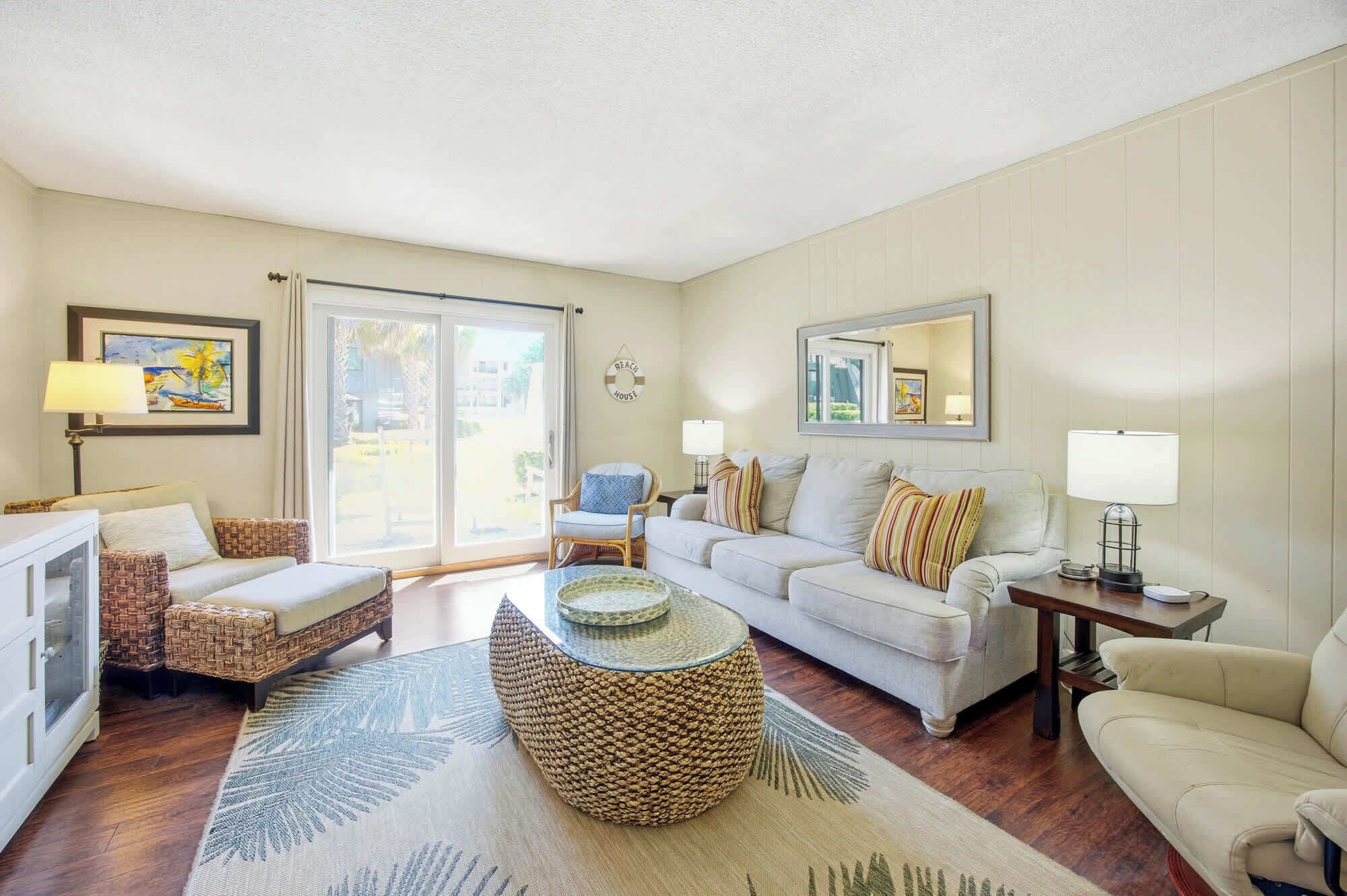 A living room with a sofa, armchairs, a coffee table, and a dining table. There is a sliding glass door leading to an outdoor area.