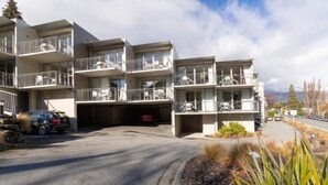 A multi-story motel with balconies, a parking area, and a mountain view. - Mountain View City Aparment (Queenstown)