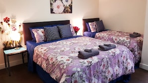 A double bed with floral bedding, a nightstand with a lamp, and a wall-mounted painting of flowers. - Mountain View City Aparment (Queenstown)