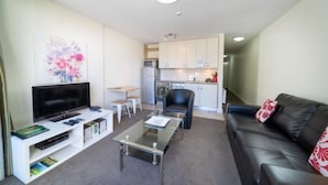 A compact living space with a TV, seating area, and kitchenette. - Mountain View City Aparment (Queenstown)