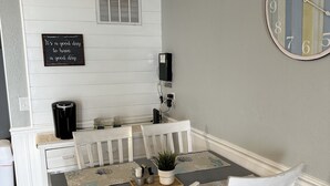 A dining area with a white table set for four, a clock on the wall, and a sign above the table. - Family Time Oceanfront Condo at Ocean Isle (Ocean Isle Beach)